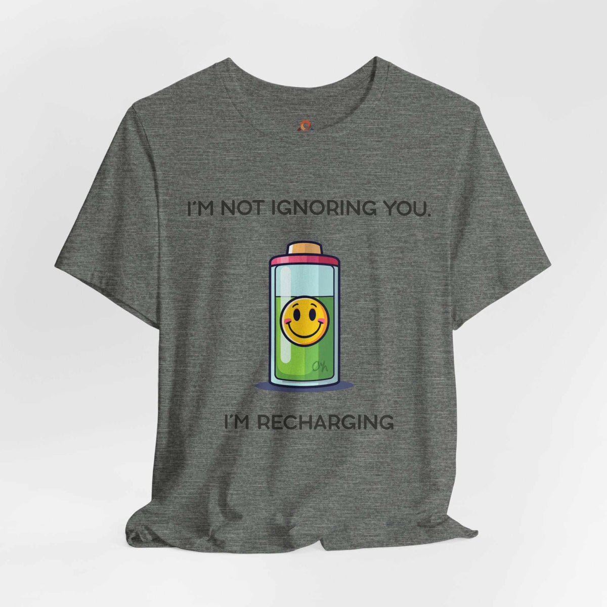 Unisex graphic t-shirt with "I'm Not Ignoring You, I'm Recharging" text and battery icon with smiley face on cream fabric